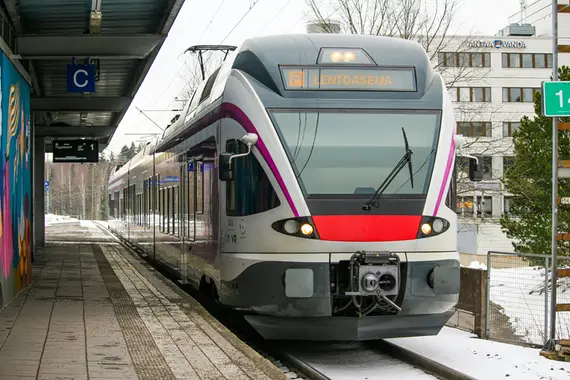 Juna Vantaalla pysähtyneenä asemalle. Juna on matkalla lentoasemalle ja taustalla näkyy rakennuksia.